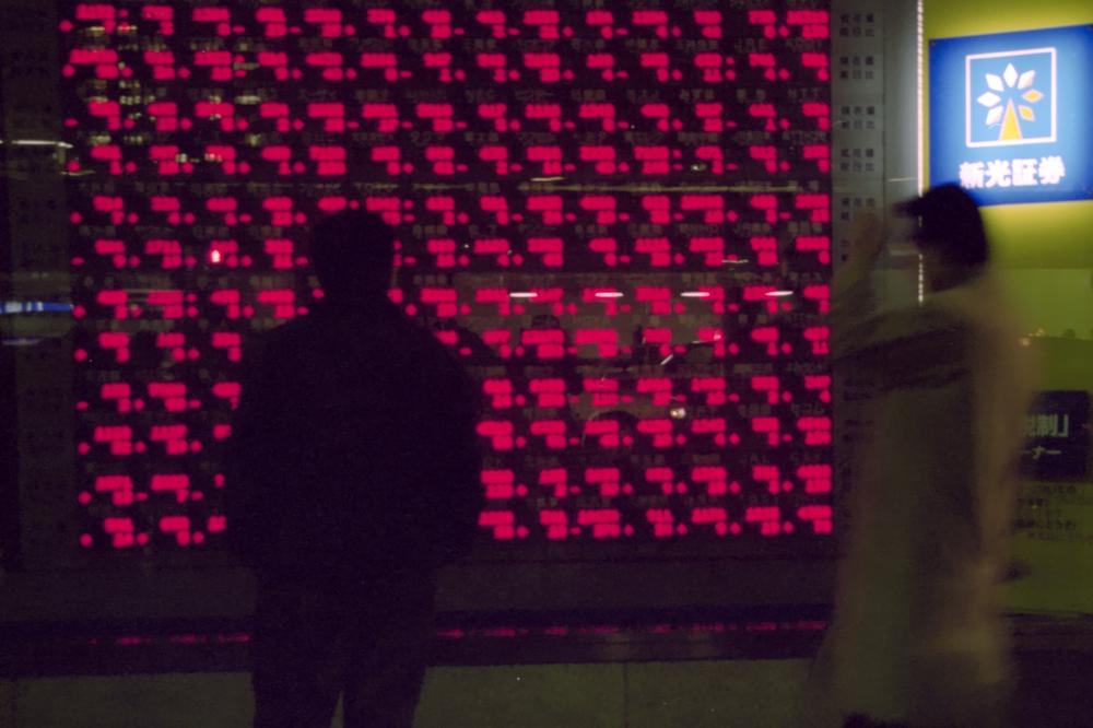 Un homme consulte les cotes boursières dans la vitrine de l'édifice de Shinkō Securities.