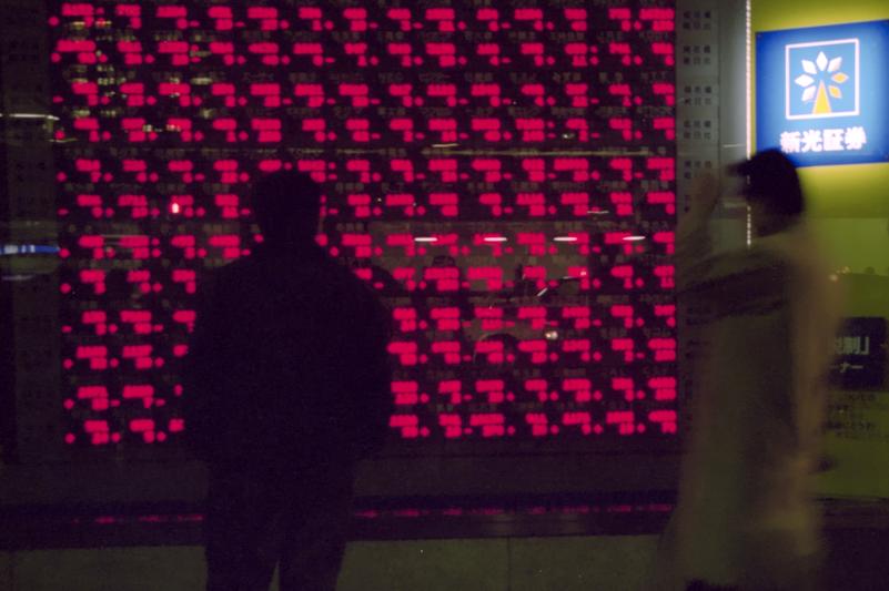 Un homme consulte les cotes boursières dans la vitrine de l'édifice de Shinkō Securities.